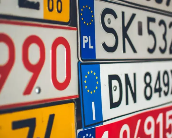 Zbliżenie na stos tablic rejestracyjnych z różnymi kody samochodowe. Widoczne numery to m.in. 990, SK 532HH, DN 849XJ.