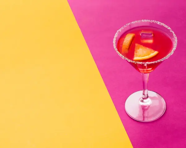 Elegancki cosmopolitan drink co zamiast żurawiny, z pomarańczą i lodem, na tle żółto-różowym.