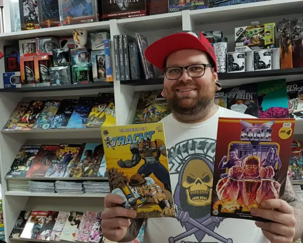 Mann mit Brille und roter Kappe hält zwei Comics in einem Comicladen.