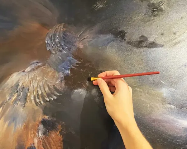 Une main tient un pinceau rouge, ajoutant des touches de lumière à une peinture à l'huile complexe d'un ange. La peinture à l'huile, c'est bien difficile, mais le résultat est saisissant.