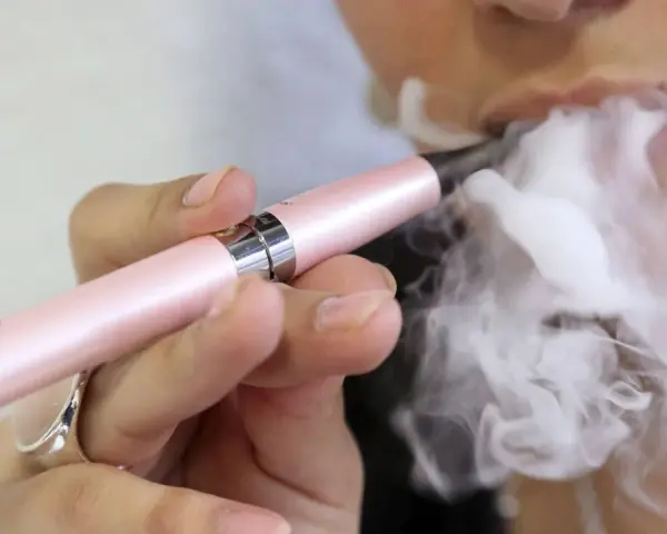 Persona vapea con un dispositivo rosa, liberando vapor. ¿Qué pasa si fumas vaper con nicotina?