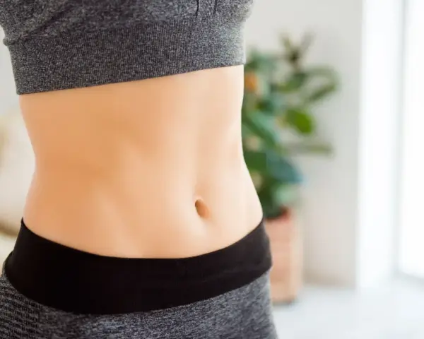 Szczupły brzuch, bez śladu wzdęty brzuch na dole. Widoczny pępek i fragment sportowego stroju.