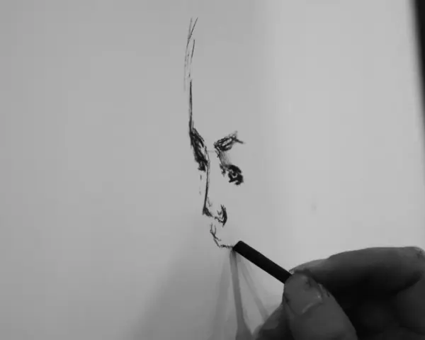 Dłoń artysty tworzy portret węglem. Każda prosta kreska buduje twarz, uchwyconą w momencie tworzenia.