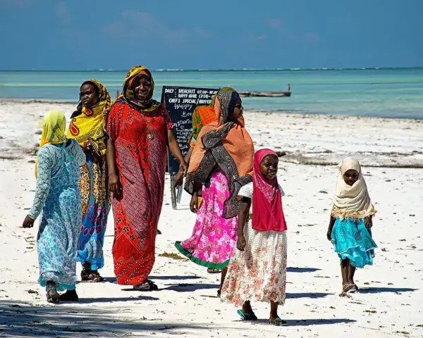 Kobiety w kolorowych strojach spacerują po plaży. Czy Zanzibar to państwo? Tak, to autonomiczny region Tanzanii, znany z pięknych plaż.