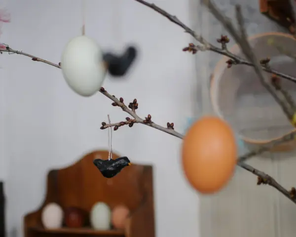 Påskris med ägg och små fåglar av papier maché. En rosa fjäder sticker upp.