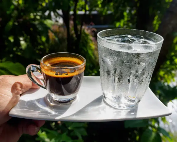 Espresso i szklanka wody z lodem na białym talerzyku. Woda do espresso przed czy po?