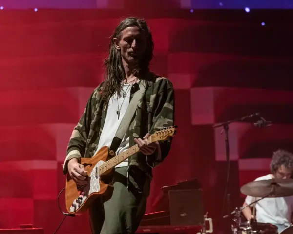 Nick Valensi spielt Gitarre auf einer Bühne, im Hintergrund ein Schlagzeuger.