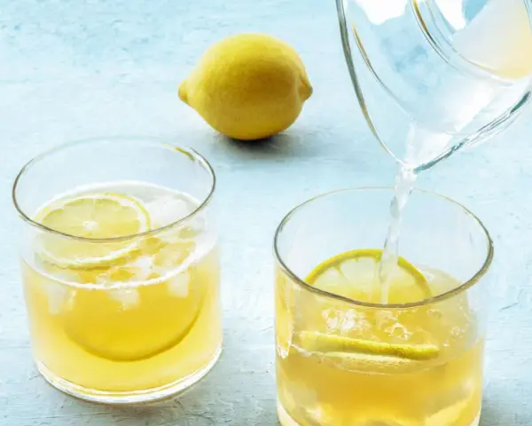 Erfrischendes zitronenwasser am morgen wird in ein Glas mit Eis und Zitronenscheiben gegossen. Eine ganze Zitrone liegt daneben.