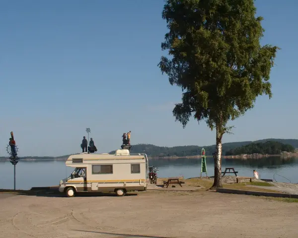 Husbil vid vattnet med figurer på taket, redo för året runt camping. En vacker plats för avkoppling.