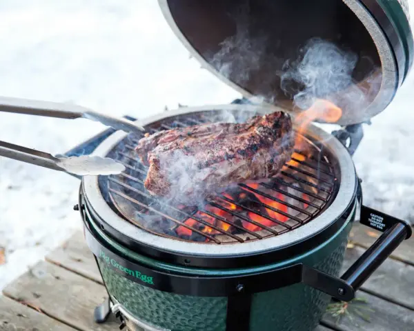 Un succulento bistec a la fiorentina cuoce sulla griglia di un Big Green Egg, circondato da fumo e fiamme.