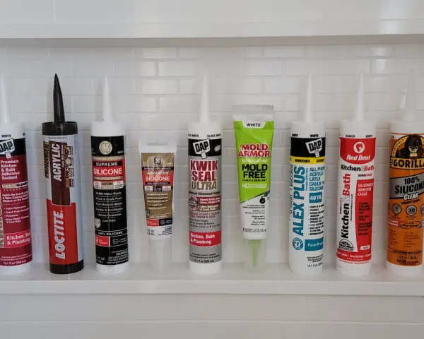 A variety of caulking tubes are lined up, ready for anyone wanting to learn how to caulk a shower. Brands include DAP, Loctite, GE, Mold Armor, Alex Plus, Red Devil, and Gorilla.