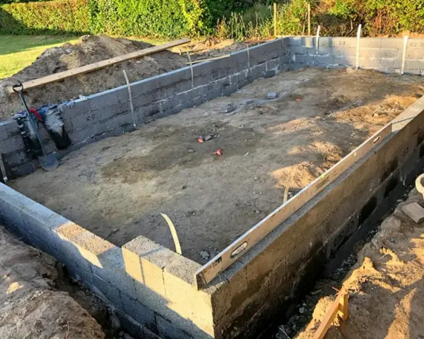 Byggarbetsplats med ett mura grund av betongblock. Schakt, spade och vattenpass syns.