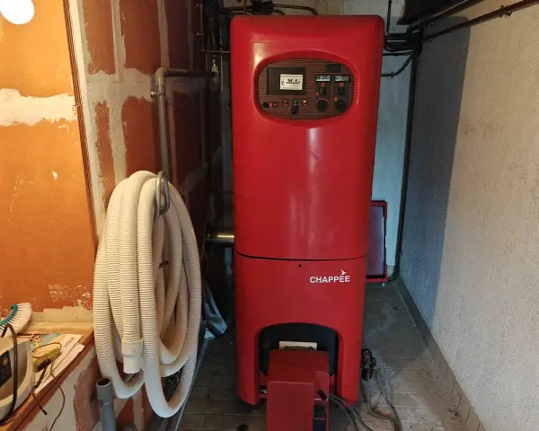Chaudière rouge Chappée dans une pièce. Un tuyau blanc enroulé est accroché au mur. Pensez à l'assurance chaudière pour votre confort.