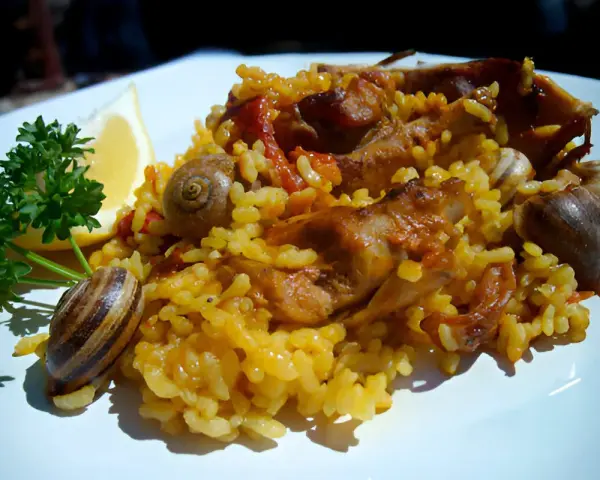 Arroz con conejo, un plato tradicional con trozos de carne dorada, arroz amarillo y caracoles, adornado con perejil y limón.