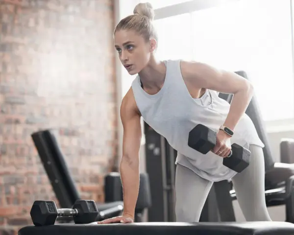 Kvinna tränar med hantlar på gym, fokuserad på att bygga muskler och gå upp i vikt.