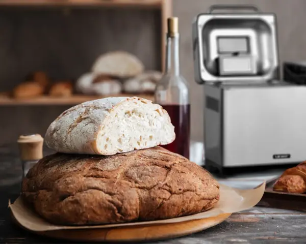 Chrupiący chleb z automatu, świeżo upieczony, czeka na śniadanie. Obok butelka wina i croissant.