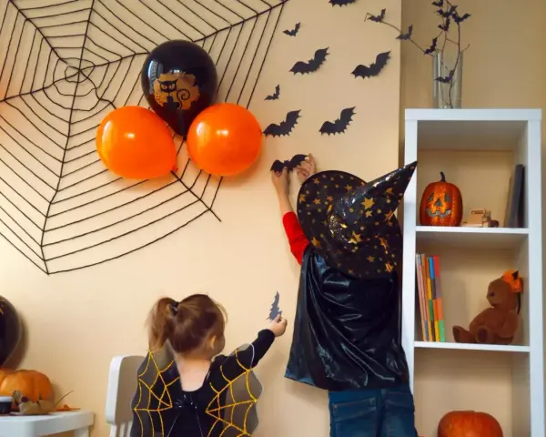 Dzieci tworzą **dekoracje halloween diy**: wieszają nietoperze na ścianie, obok pajęczyny i balonów.