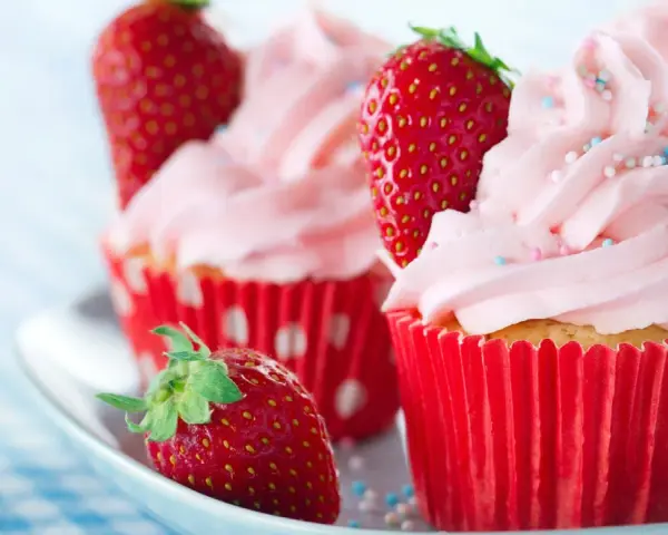 Erdbeer cupcakes mit rosa Zuckerguss und frischen Erdbeeren, verziert mit bunten Streuseln.