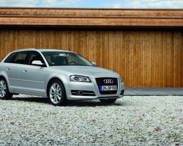 Silberner Audi A3 Baujahr 2008 steht auf einem Kiesparkplatz vor einer Holzwand.