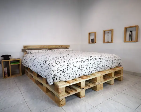 Un letto fai da te economico realizzato con pallet di legno, con un copriletto bianco e nero a tema alfabetico.