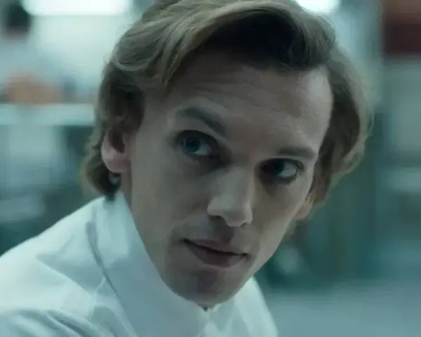 Henry Creel, znany jako Vecna z 001 stranger things, w białej koszuli, patrzy z uwagą.