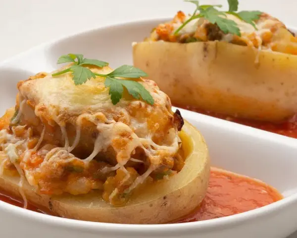 Patatas rellenas de carne de la abuela, gratinadas con queso y perejil, servidas con salsa de tomate.