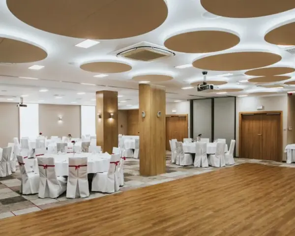 Elegancka sala bankietowa gotowa na wesele we wrześniu. Okrągłe stoły z białymi pokrowcami i czerwonymi wstążkami czekają na gości.