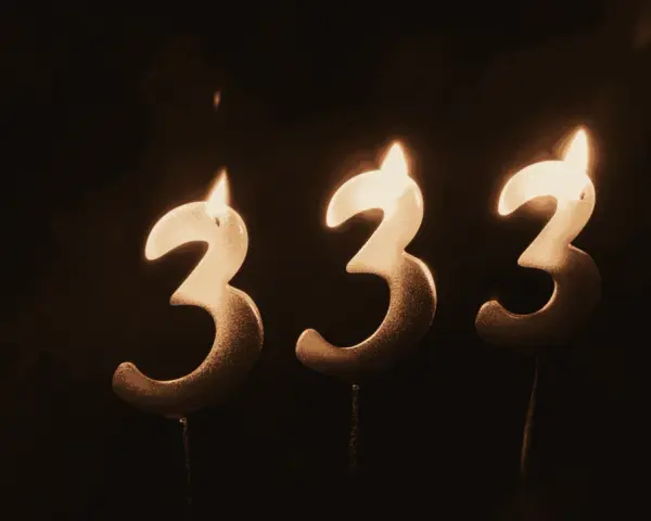 Trzy świeczki w kształcie cyfry 3, płonące w ciemności. Liczba 333 znaczenie, symbolizująca harmonię i równowagę.