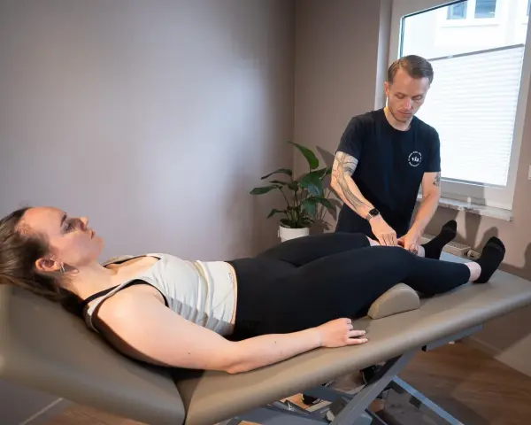 Therapeut führt Lymphdrainage am Bein einer liegenden Frau durch. Die Frage "wie lange dauert eine lymphdrainage" wird hier beantwortet.