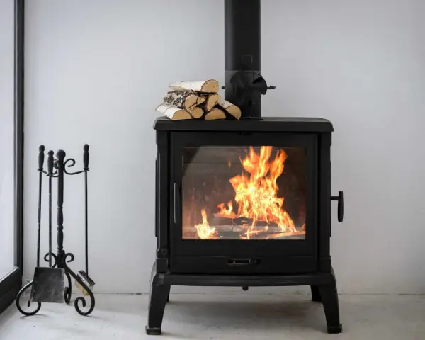 Estufa de leña con fuego vivo, lista para canalizar aire y chimenea. A su lado, un atizador y escoba.