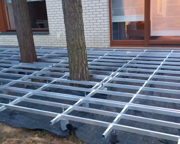 Konstrukcja pod wysoki taras z deski kompozytowej, z drzewami przechodzącymi przez ruszt.