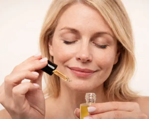 Kobieta z zamkniętymi oczami aplikuje serum z **retinolem**, dbając o skórę, by uniknąć efektów **solarium**.