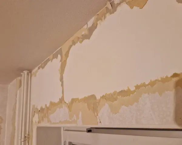 Tapeten flagnar och visar lager av gammal färg och papper. En renovering är på gång, där man förbereder för att måla på tapet.