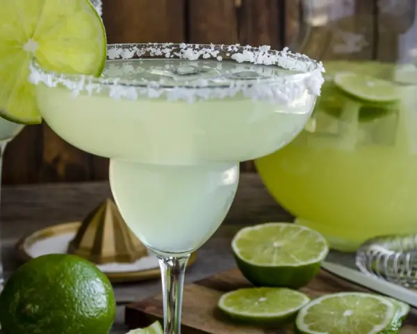 Spicy Margarita przepis: orzeźwiający drink z solą na brzegu kieliszka, limonkami i dzbankiem pełnym zielonego napoju.