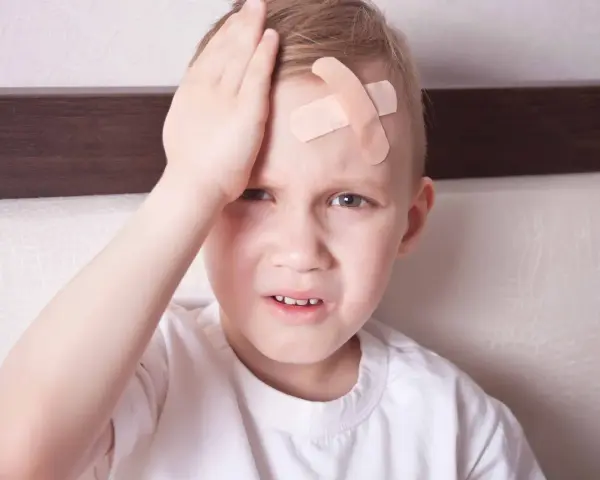 Chłopiec z plastrem na czole, zmartwiony, może to być objaw wstrząsu mózgu u niemowlaka.