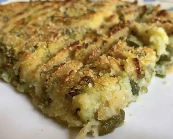 Fetta di polpettone genovese, con patate e verdure verdi, cotto al forno e cosparso di pangrattato croccante.