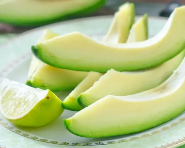 Plasterki awokado i ćwiartka limonki na talerzu. Awokado jest bogate w zdrowe tłuszcze, witaminy i minerały, co sprawia, że ma wiele korzystnych właściwości.