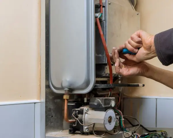 Mani che riparano uno scaldabagno a gas: il bruciatore non parte. Si vede il tecnico con un cacciavite blu.
