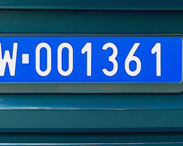 Niebieskie tablice rejestracyjne z numerem W-001361 na ciemnozielonym samochodzie.