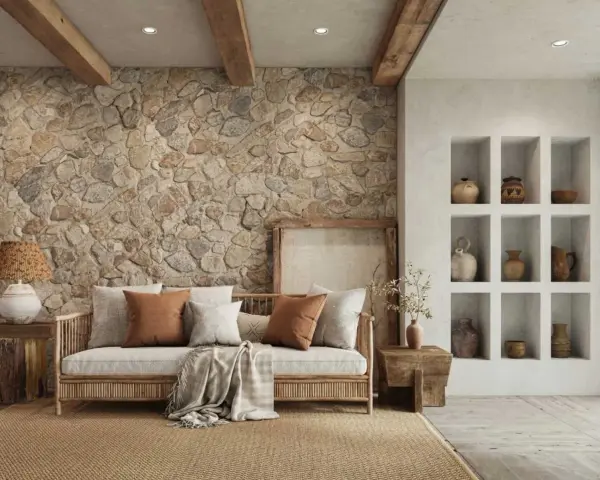 Sofá de madera con cojines y manta, junto a una pared con acabado rústico de piedra y vigas de madera.
