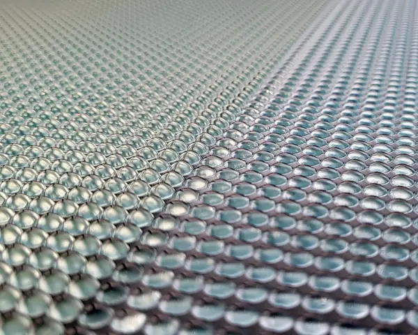 Close-up of a 3d printed lens array, with rows of tiny, clear, dome-shaped lenses reflecting light.