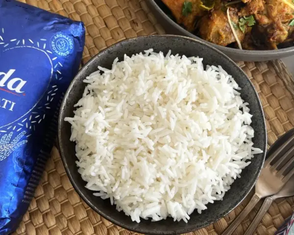 Un tazón de arroz basmati blanco y esponjoso junto a un paquete de Tilda Basmati Original.
