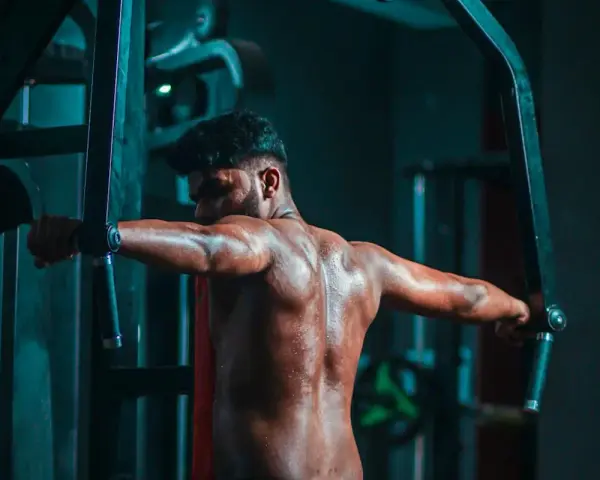 Man svettas under ett träningspass med flyes med hantlar i ett mörkt gym.