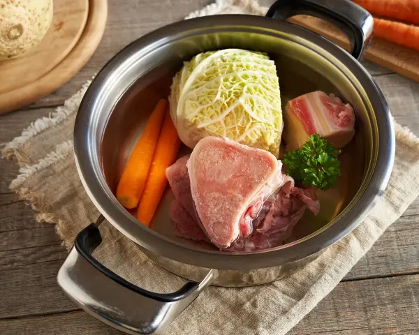 Une marmite remplie d'ingrédients pour une potee au chou : chou, carottes, viande et os.