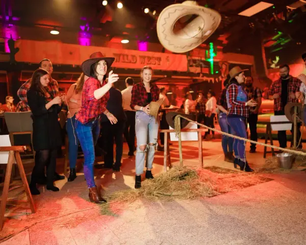 Impreza w stylu country: kobiety w kratkach i kapeluszach rzucają kapeluszem do celu.