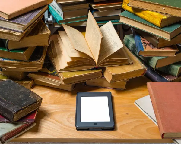 Stosy starych książek i nowoczesny ebook na drewnianym blacie. Wybór między tradycją a technologią.