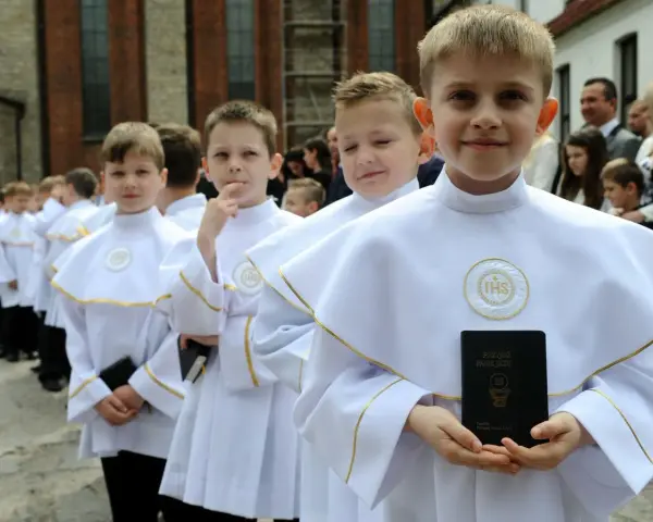 Chłopcy w białych albach, gotowi do komunii, trzymają modlitewniki. Jeden z nich uśmiecha się do aparatu.