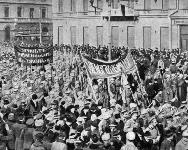 Multitud con pancartas y uniformes militares marchando en una calle, con edificios al fondo.