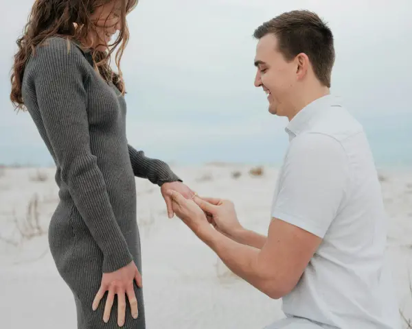 Mann macht Heiratsantrag am Strand. Ab wann darf man sich verloben? Das ist eine Frage der Liebe, nicht des Alters.