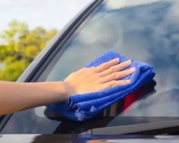 Mano con paño azul limpiando los cristales del coche para una visibilidad perfecta.